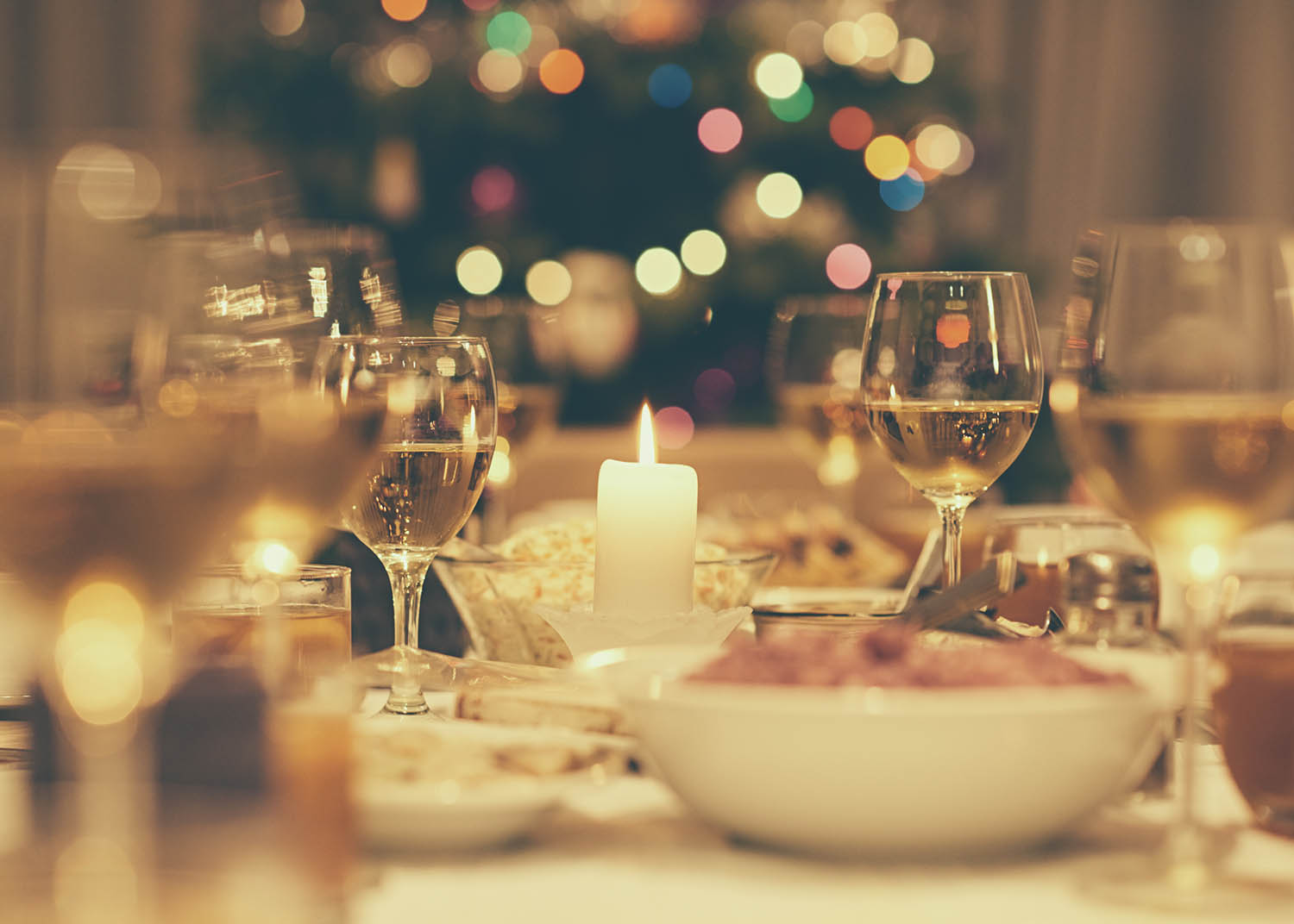 Dining table full of a variety of delicious festive food and wine with a Christmas tree in the background in home with vintage style