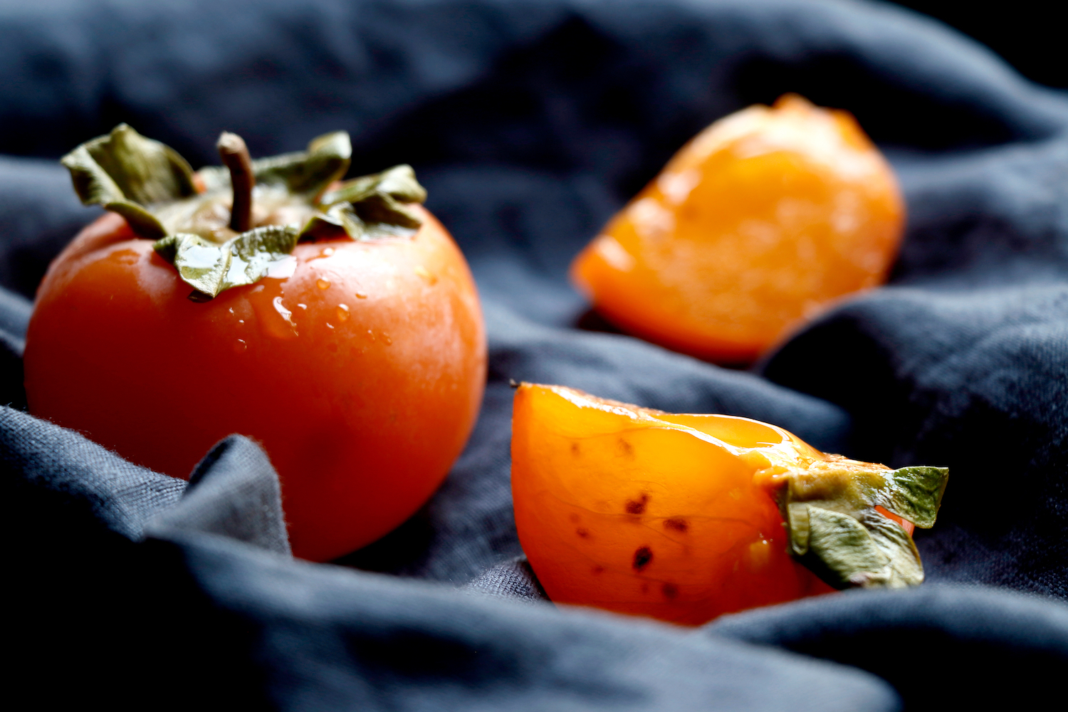 Slices of persimmon.Ripe orange persimmon fruit.Close up of fresh kaki on dark blue.Set of kaki.