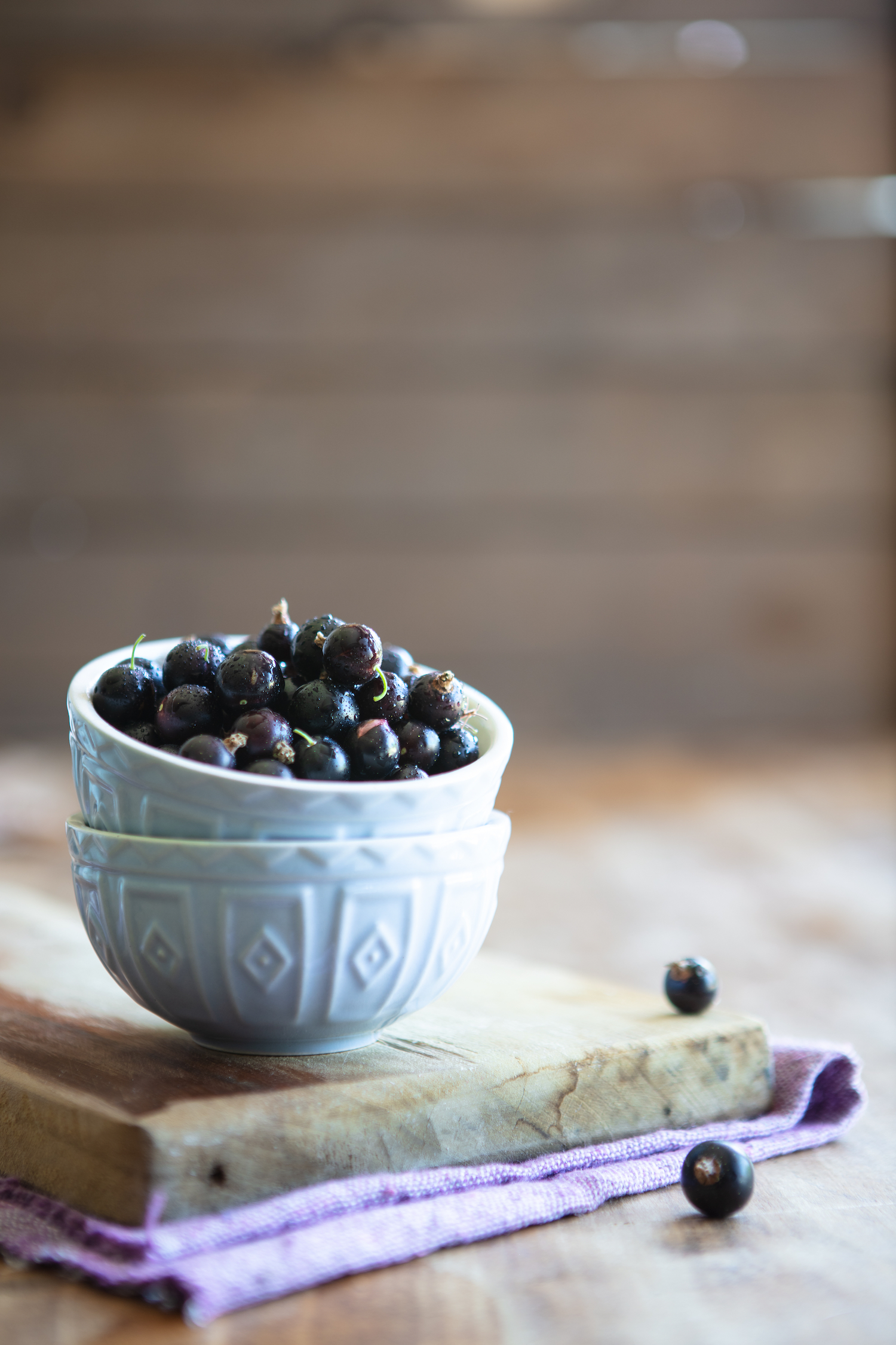 Blackcurrants stacked in a pale blue bowl in rustic setting with scattered fruit