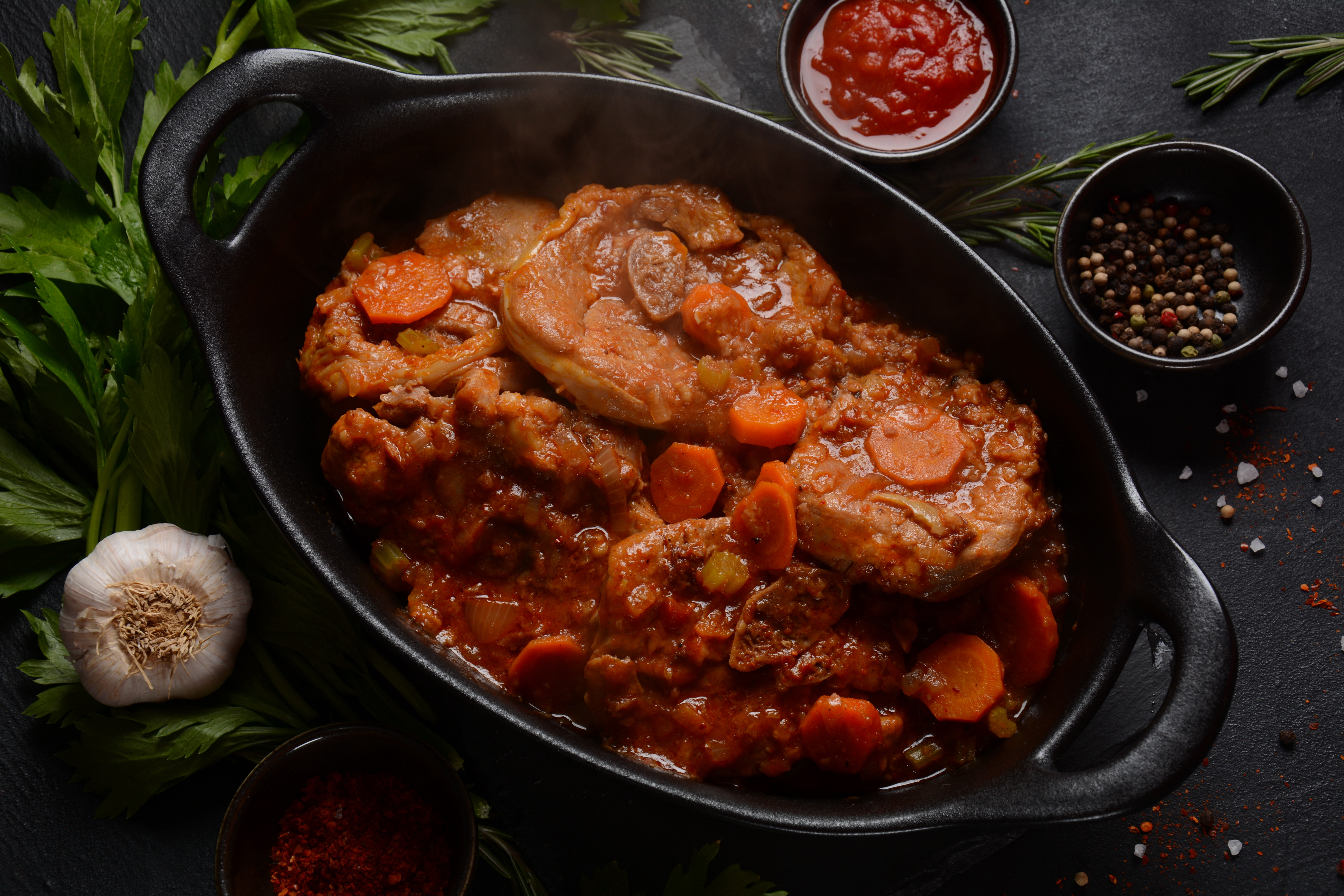 Ossobuco meat stew on the bone and vegetable sauce with carrots, tomatoes and celery in iron pan. Italian cuisine 
