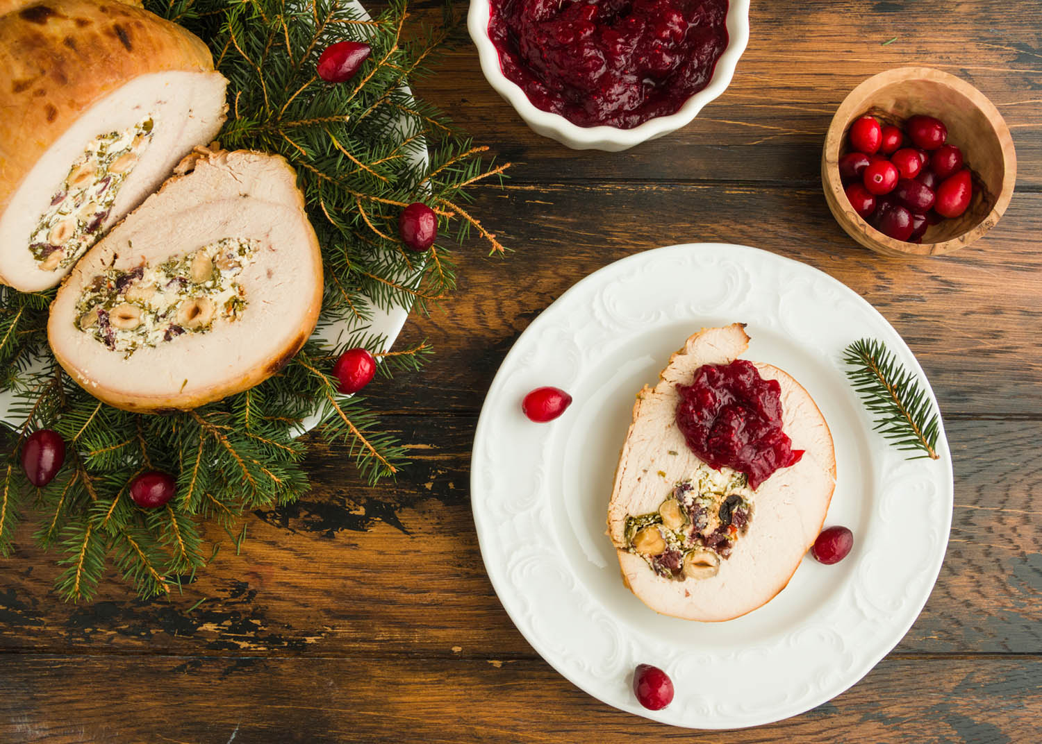 Stuffed  turkey breast roll with cranberry sauce on white plate on rustic wooden table, top view