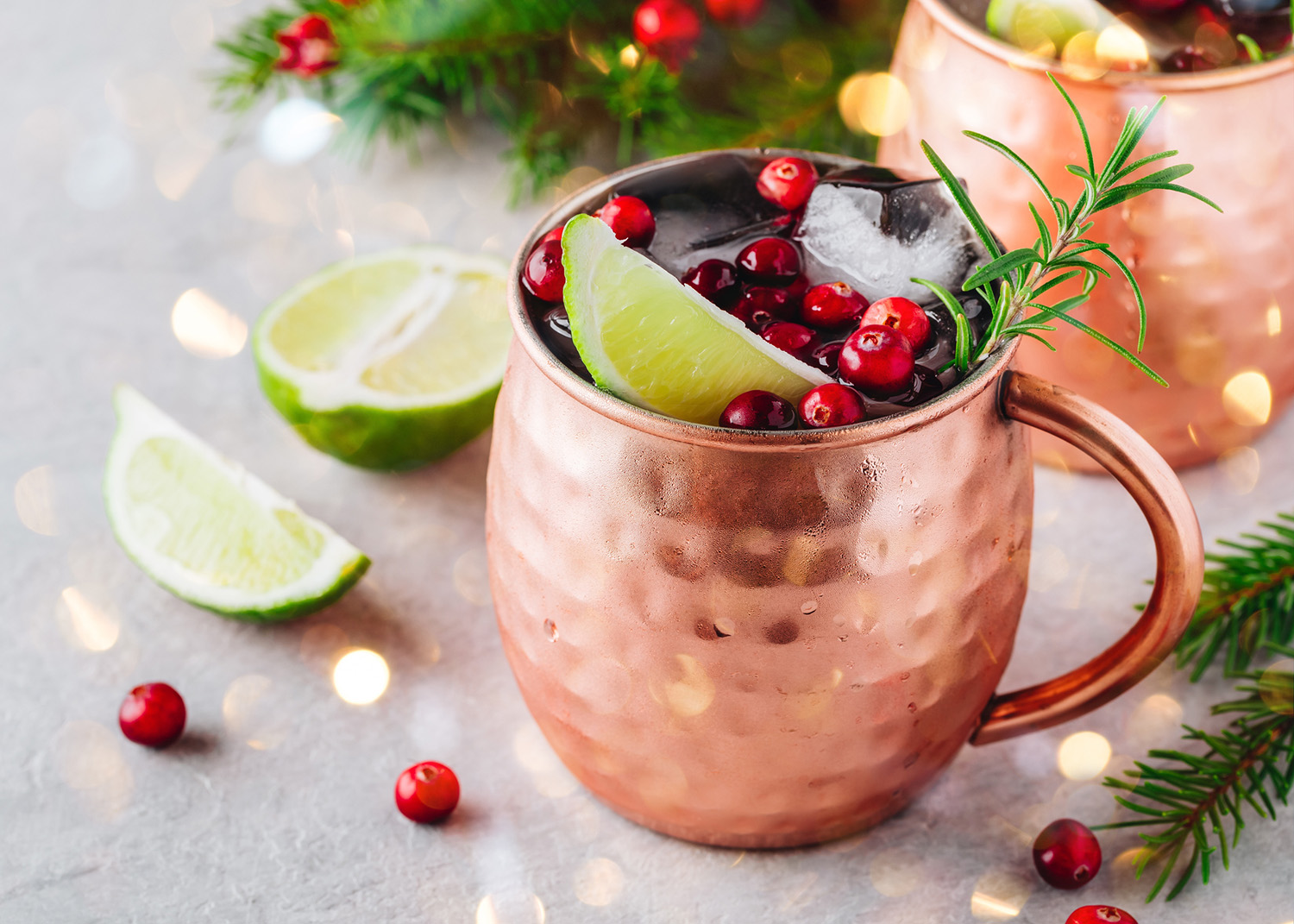 Christmas Moscow Mule ice cold Cocktail in copper cup with cranberries, lime and rosemary on gray stone background.