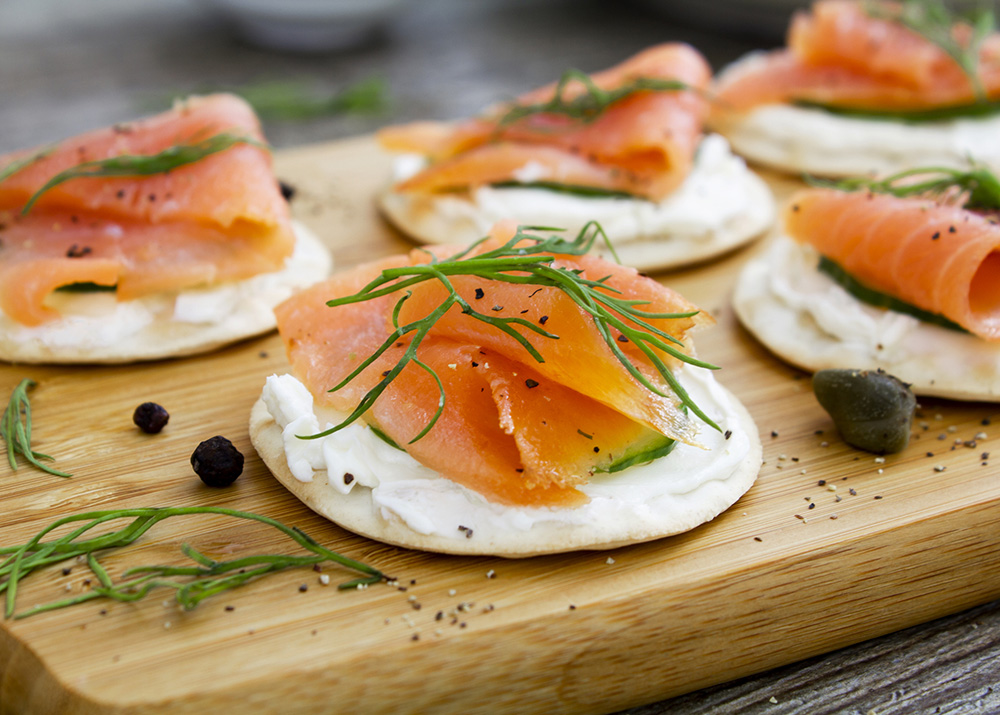 Fresh smoked salmon canapes on a wooden chopping board, with cream cheese, black pepper and dill. Shot on a wooden chopping board on a rustic wooden background. Close up.