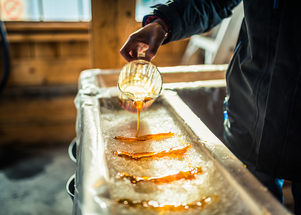 A close-up of a person at sugar shack pouring maple syrup onto snow to make maple sugar taffy