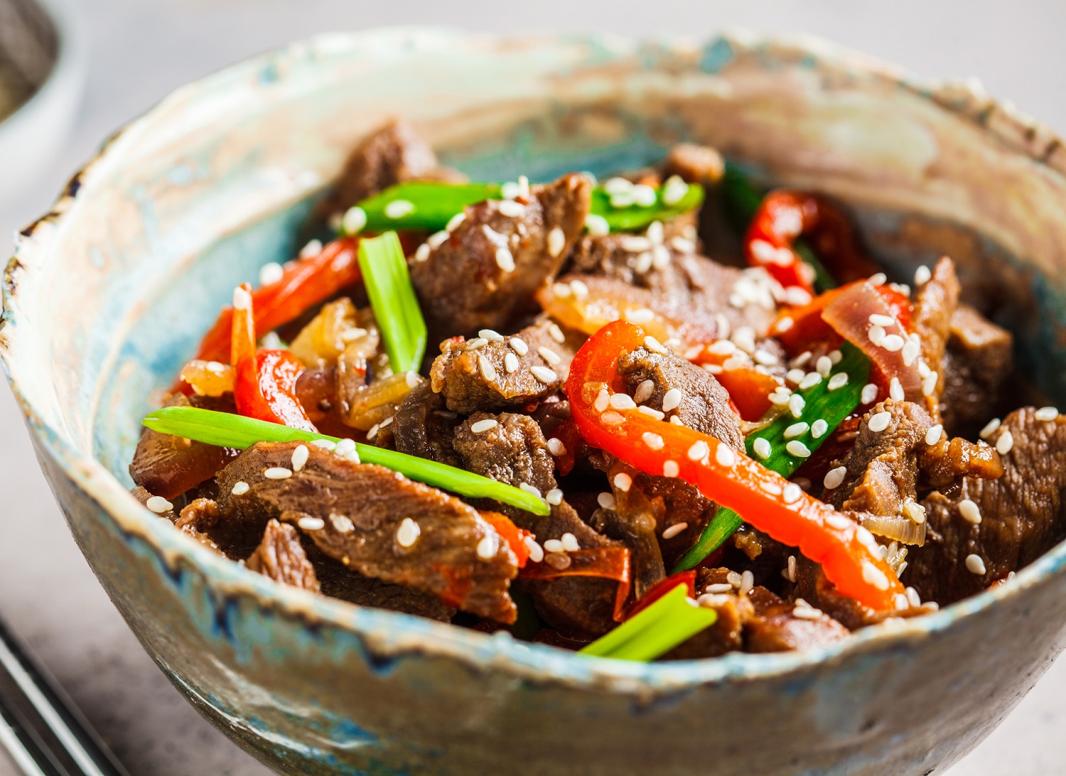 Asian teriyaki beef with green onions and sesame seeds in a beautiful bowl, gray background.
