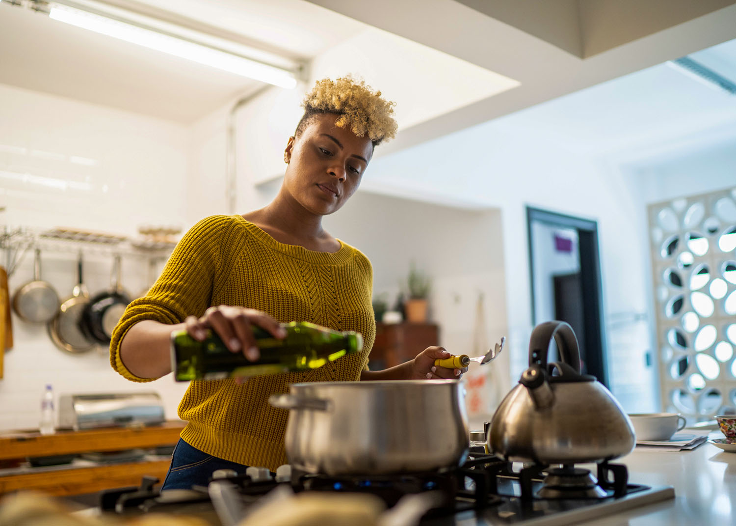 Young woman preparing food at home using olive oil