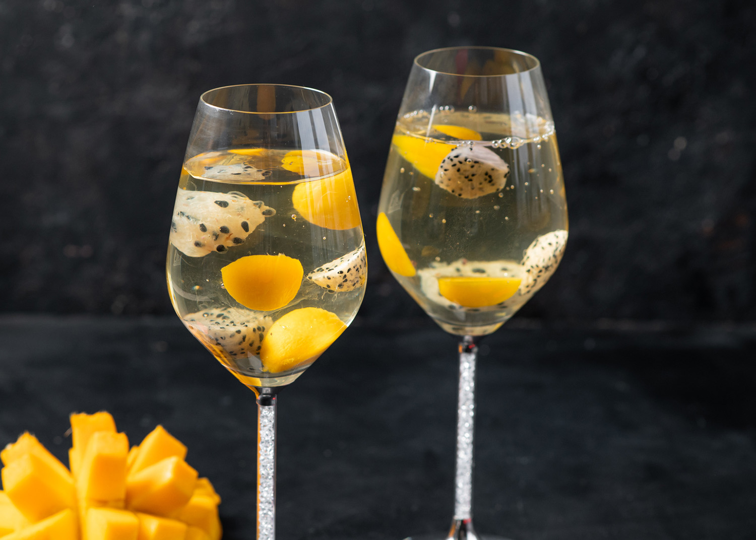 Dessert champagne jelly with exotic fruits - mango and pitahaya in a glass. On a black background