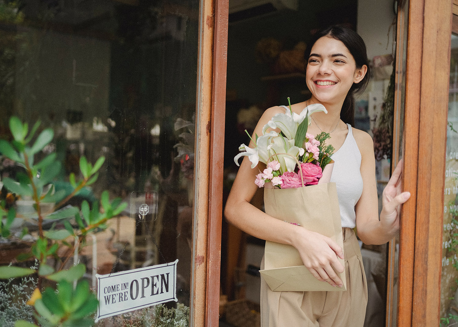 Une femme dans l'entrée d'une boutique tient un bouquet