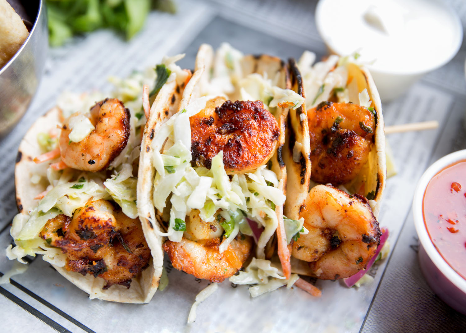 Grilled jumbo shrimp in corn tortilla tacos with cabbage garnish on an old fashioned newspaper wrapper.