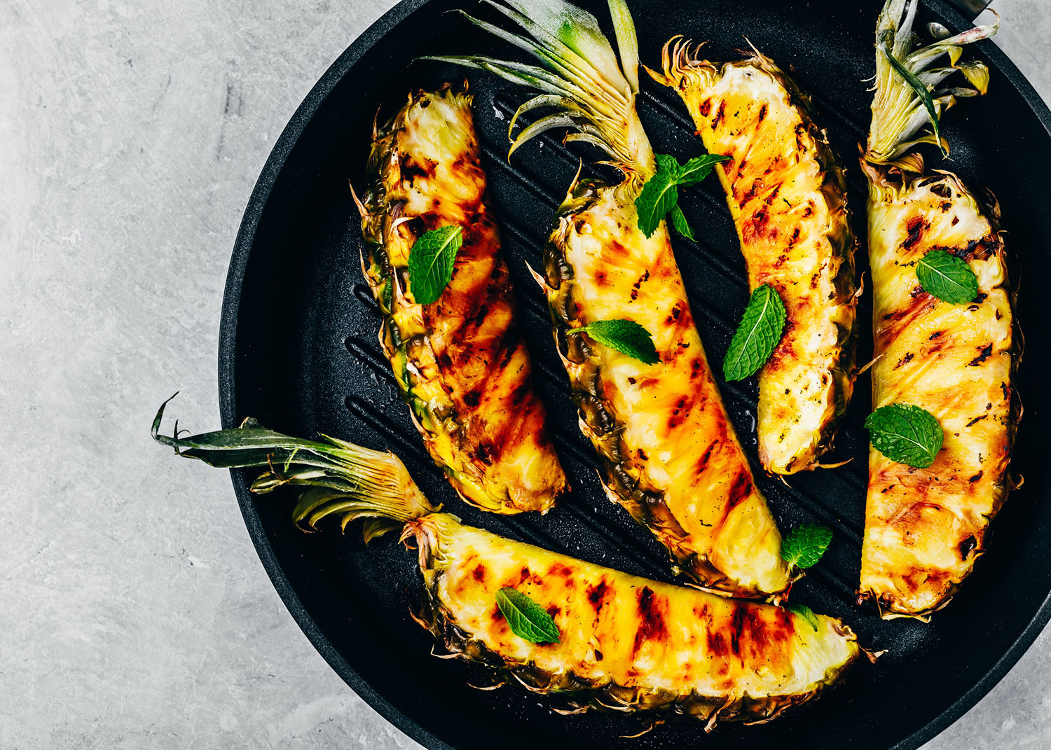 Grilled pineapple with fresh mint in cast iron pan on gray stone background. Top view, copy space