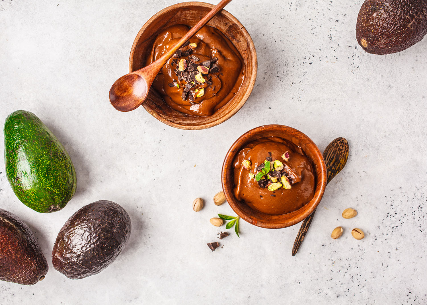 Avocado chocolate mousse with pistachios in a wooden bowl on a white background, top view, copy space.