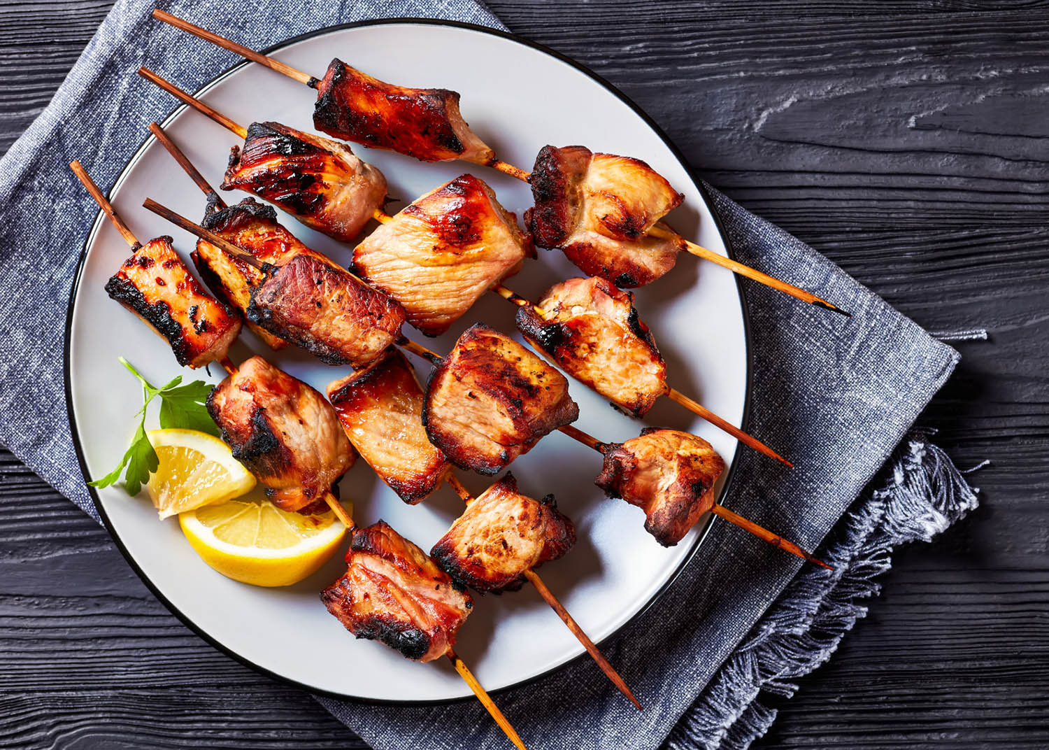 Juicy grilled pork kebabs on a plate on a black wooden table, flat lay, free space