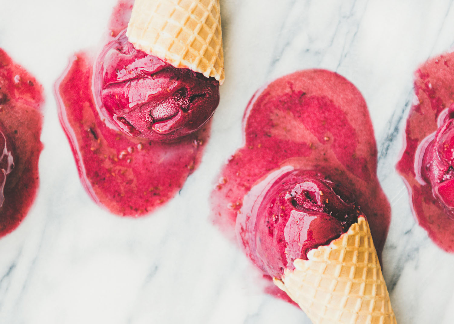 Fresh summer dessert. Flat-lay of red melting natural raspberry sorbet ice-cream scoops in sweet waffle cones over light marble background, top view, close-up. Healthy vegan sweet food