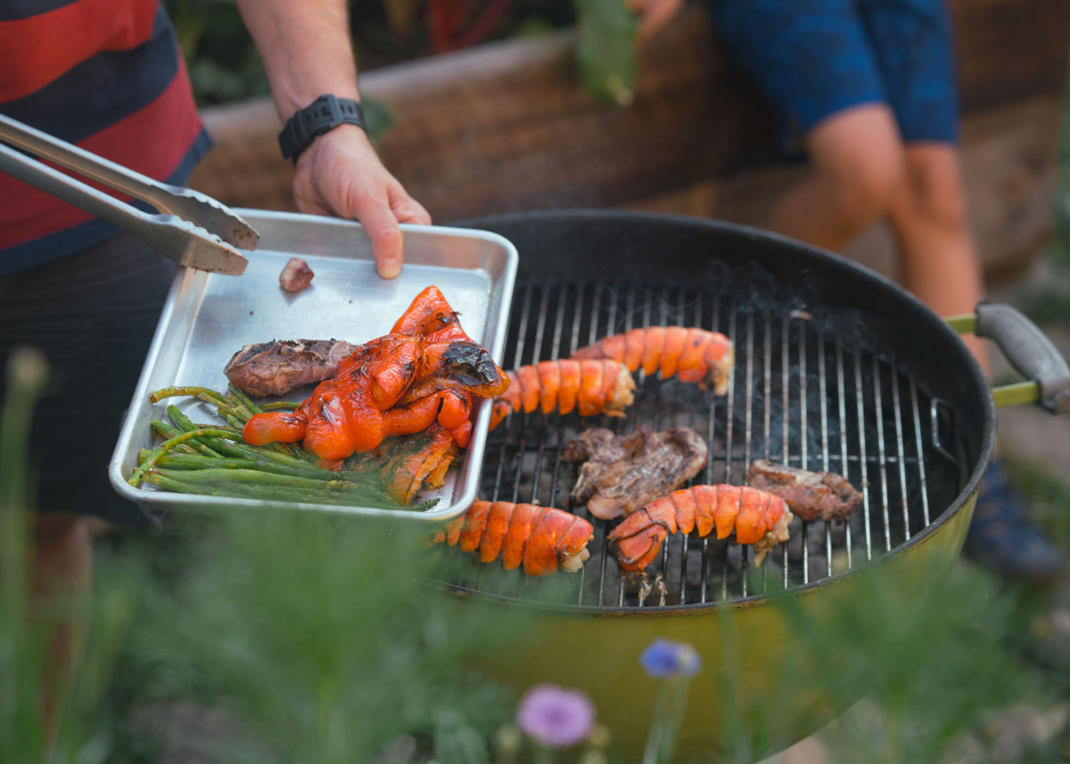 Laid-back summer day calls for a cookout with family and dog Backyard blooming with flowers.  Grilled lobster, grilled hamburger and veggies. Dog and child playing together. Laughing family, hugs exchanged, cheers to beer all add to a warm and good family dinner. Editor Adrian Walker