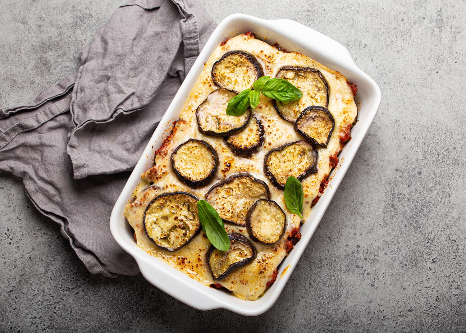 Greek mediterranean dish Moussaka with baked eggplants, ground beef in white ceramic casserole on rustic stone background from above, traditional dish of Greece