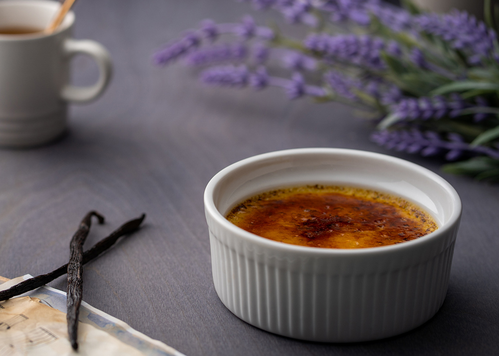Creme brulee with vanilla beans, cup of tea, book and lavender flowers on grey background