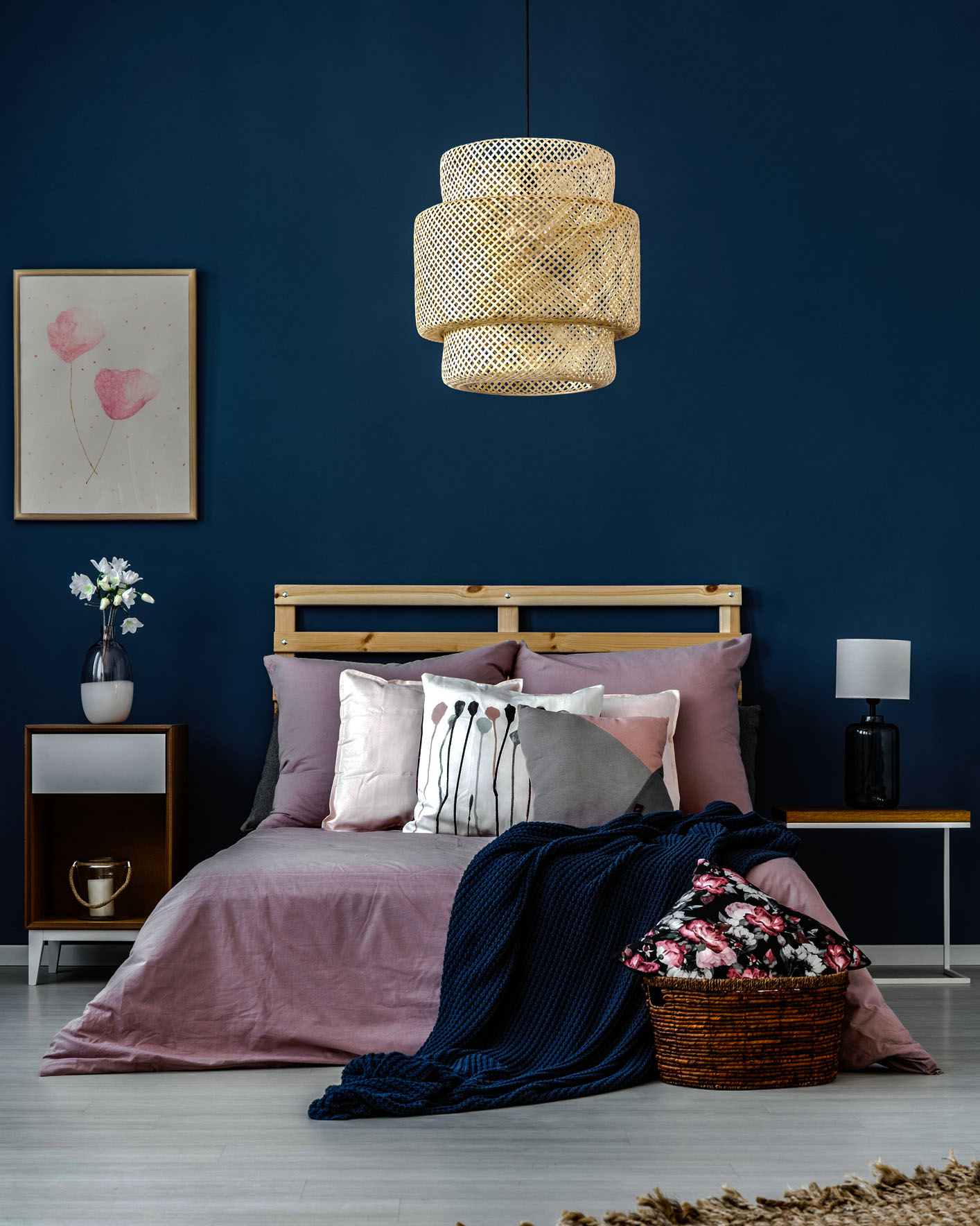 Designed lamp above king-size bed with dark blue blanket and pastel pillows in room with blue wall