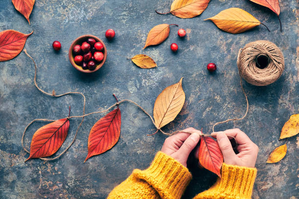 Fall decorations handmade with natural materials. Making garland with and vibrant red Autumn leaves.