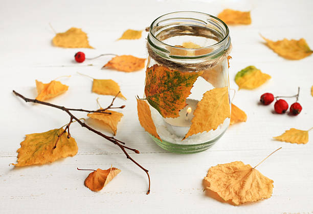 ealight candle in glass jar, decorated dried golden leaves. Fall time interior decor.