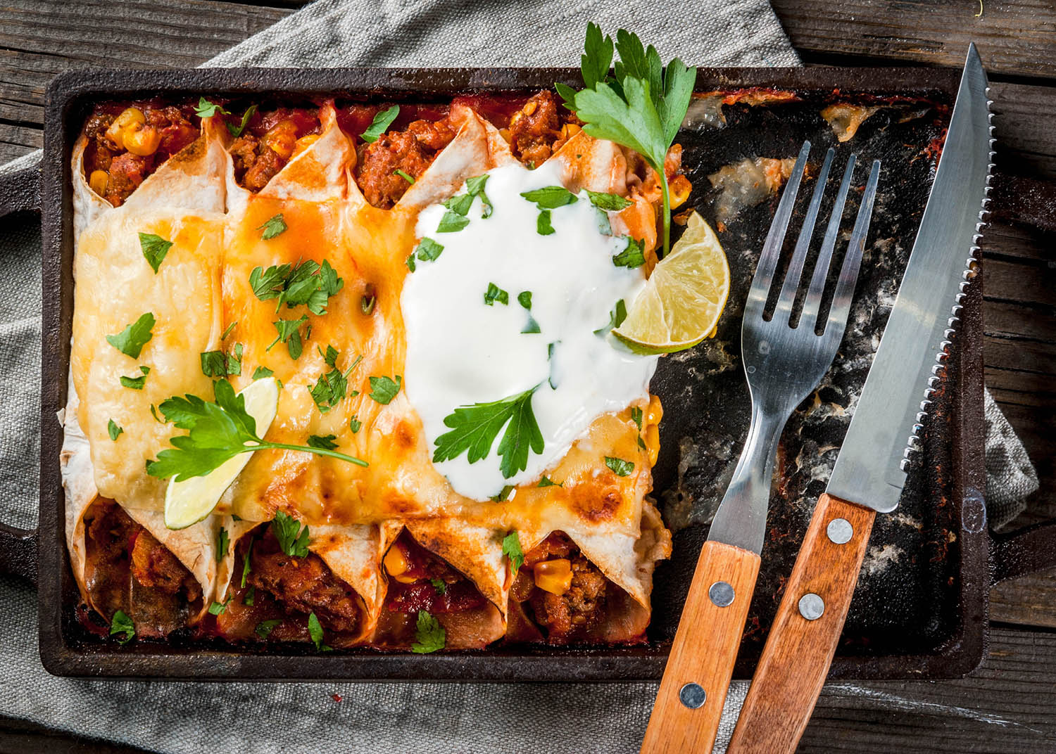 Mexican food. Cuisine of South America. Traditional dish of spicy beef enchiladas with corn, beans, tomato. On a baking tray, on old rustic wooden background. Top view