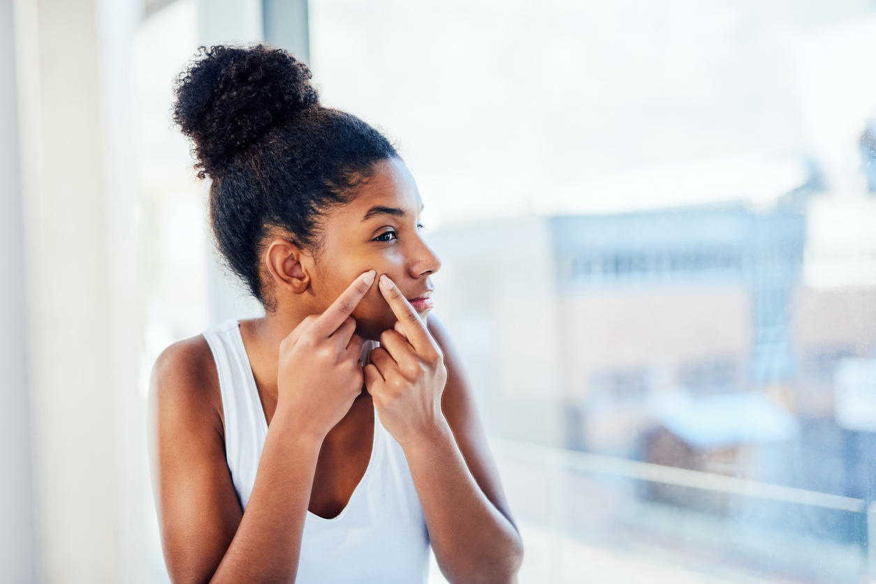 Shot of a young woman popping a pimple on her face