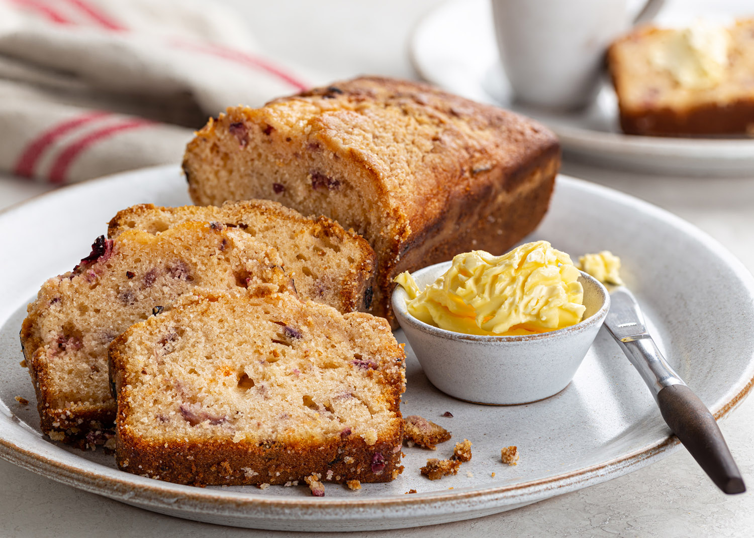 Sliced cranberry orange loaf cake and bowl of butter on a plate