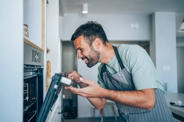Handsome young man preparing healthy meal in modern kitchen. Smiling man checking food in the oven.