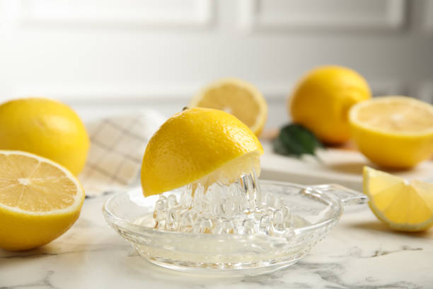 Glass squeezer and fresh lemons on white marble table