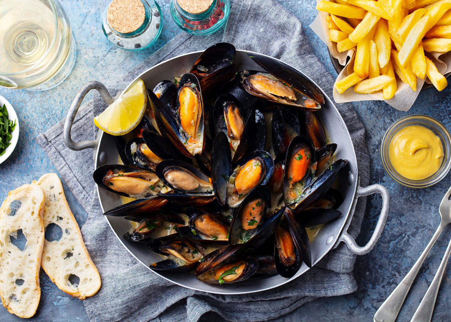 Mussels with french fries and white wine in cooking pan. Grey background. Close up. Top view.