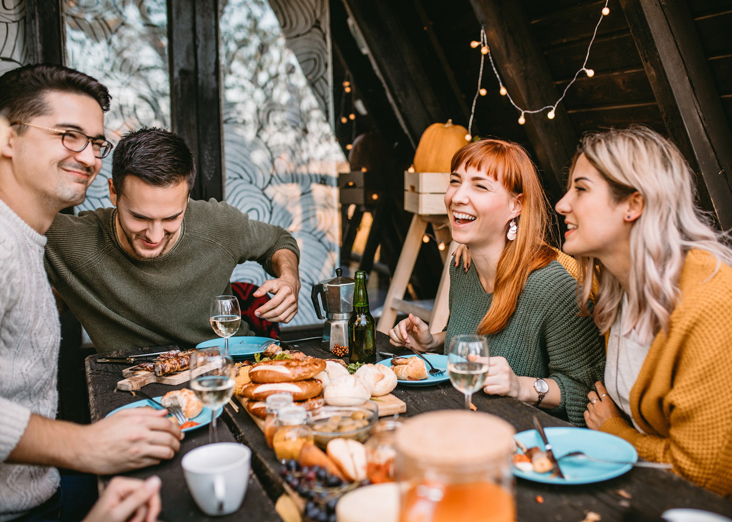 Group of smiling friends enjoys food and conversation at autumn picnic at weekend house