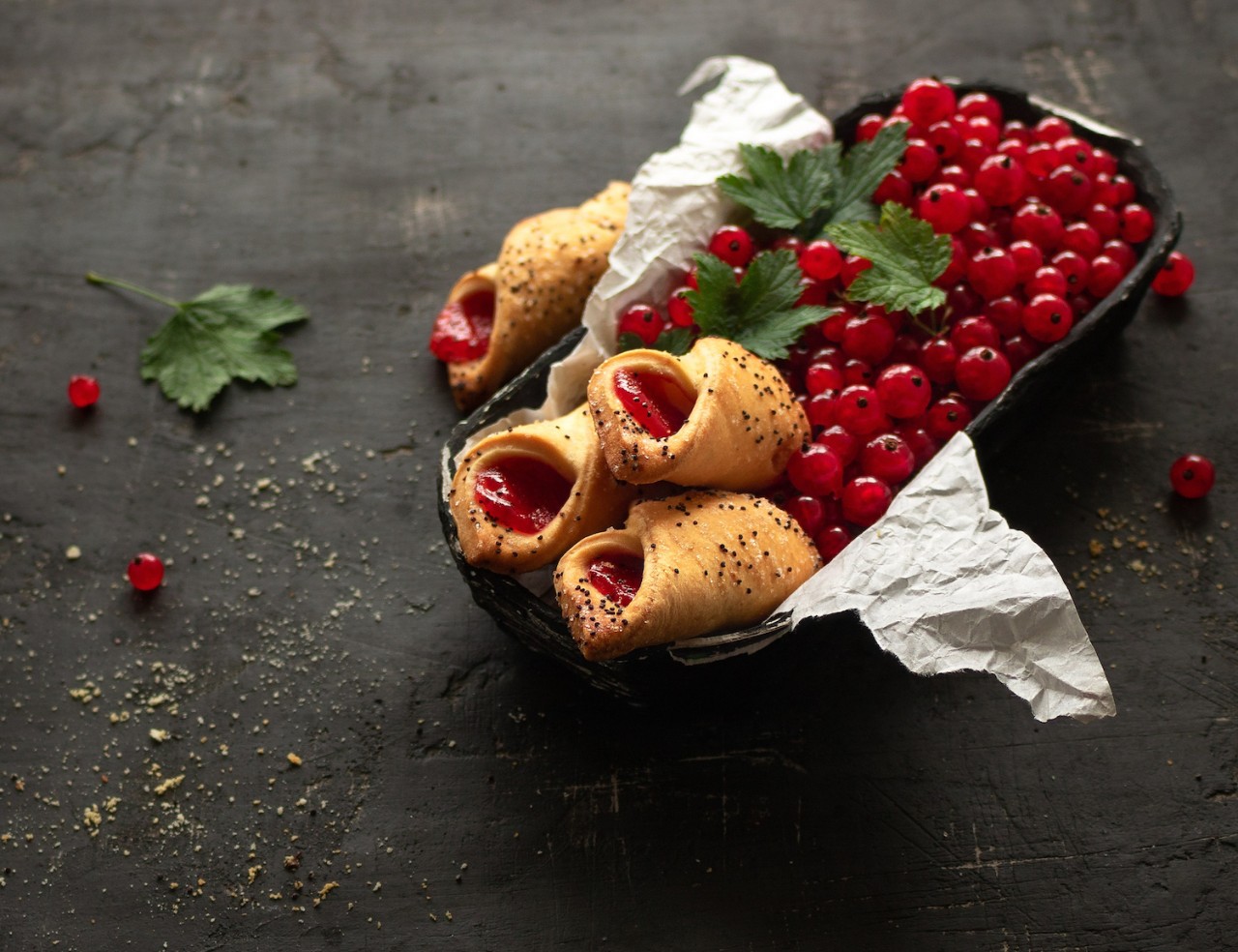 Shortbread envelope cookies with redcurrant jam and ripe redcurrant in a box on a black background.