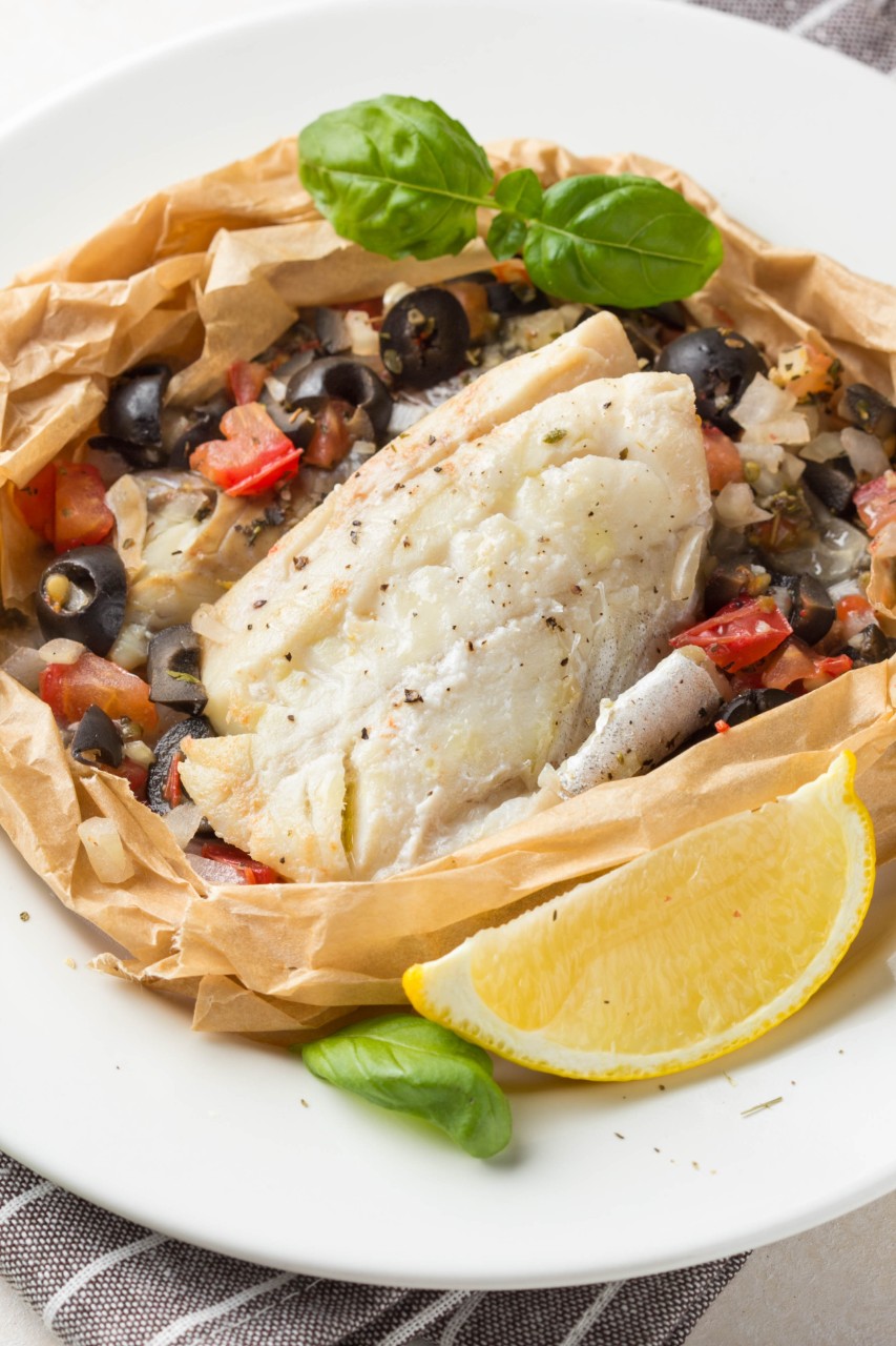 Fillet of white fish (Pollock, cod, sea bass, Dorada) with olives, tomatoes and lemon, baked in parchment. Traditional French food fish papillot with bulgur