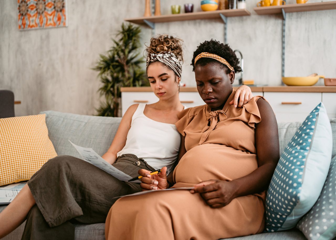 Young beautiful black pregnant woman and her partner sitting on the sofa in the living room, checking and discussing their finances