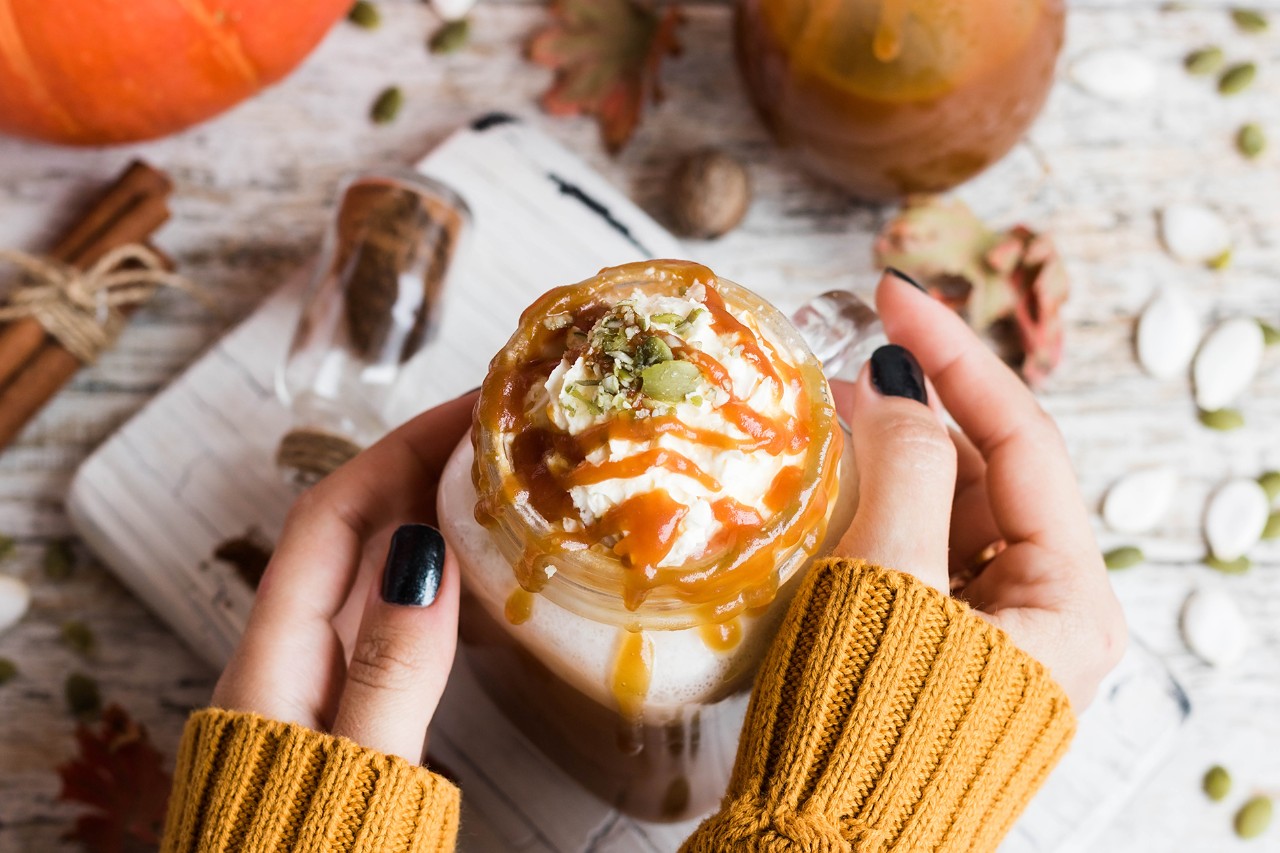 Spicy pumpkin latte with spices and a cap of whipped cream decorated with salted caramel and crushed pumpkin seeds