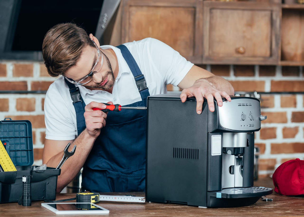 professional young worker in eyeglasses and protective workwear fixing coffee machine 