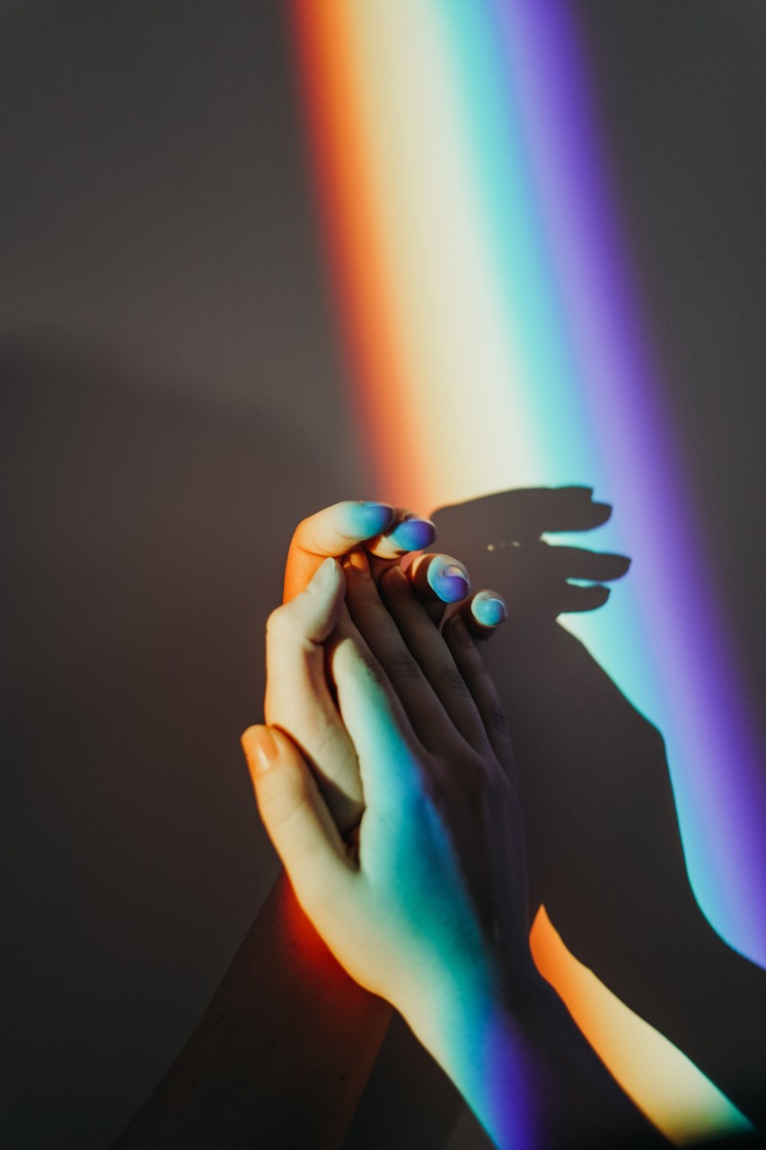 Deux mains se touchent devant un faisceau de lumière arc-en-ciel