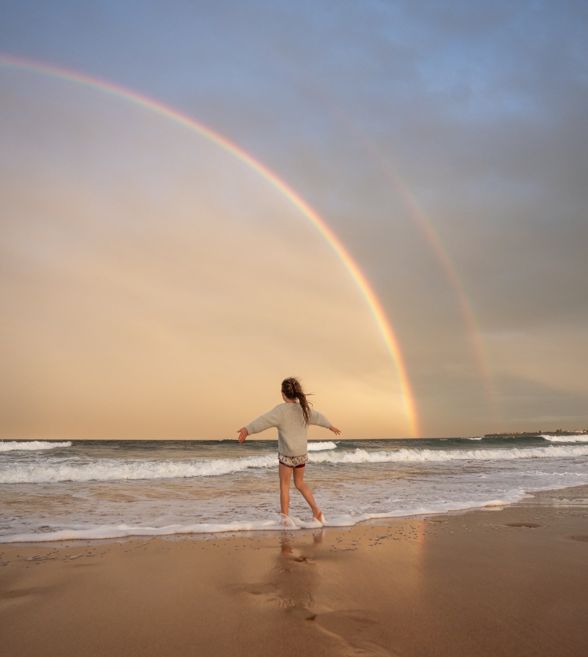Jeune femme sur la plage avec un arc-en-ciel