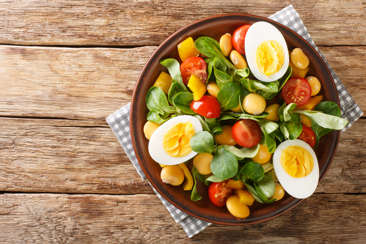 Breakfast of boiled eggs and salad of lupine beans, tomatoes and common cornsalad close-up in a plate on the table. horizontal top view from above