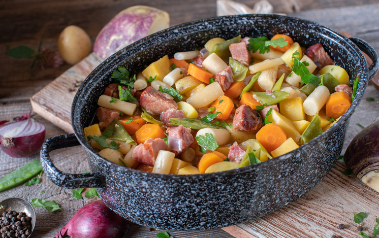 Healty savory meat stew served in a rustic pot with root vegetables on wooden table. Closeup view from above
