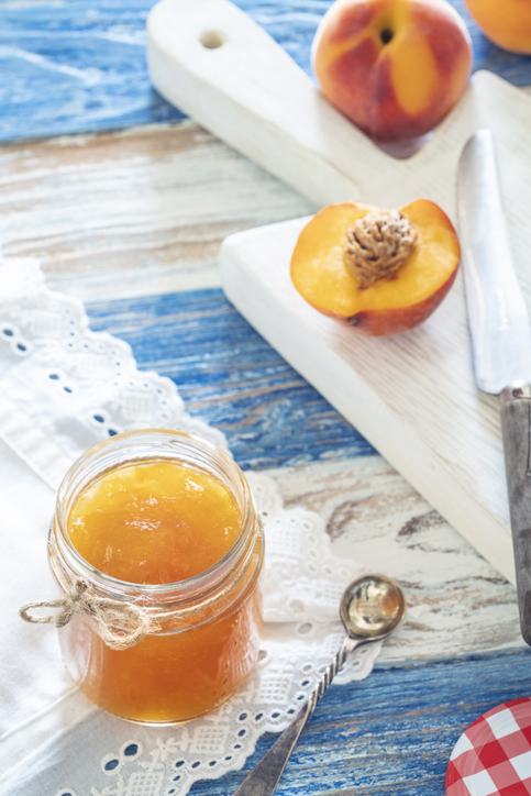 Peaches jam homemade glass pot with peach fruits on cutting board in white and blue background