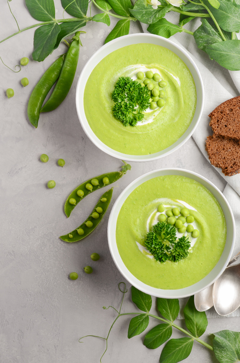 Green pea soup in bowls on grey concrete or stone background, top view