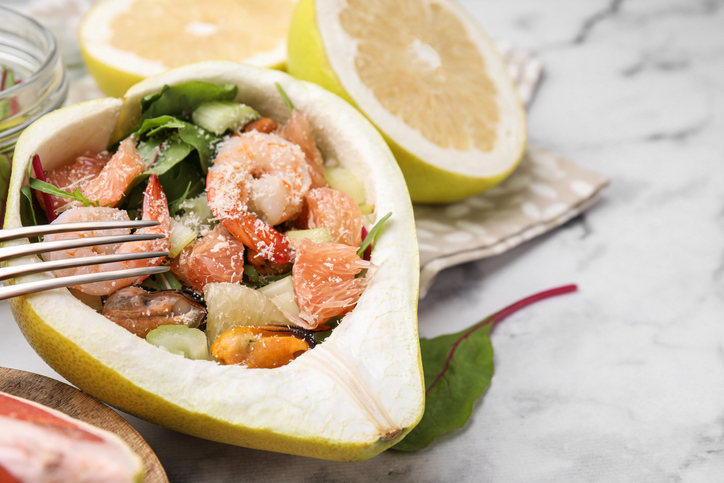 Delicious pomelo salad with shrimps in half of fruit on white marble table, closeup. Space for text