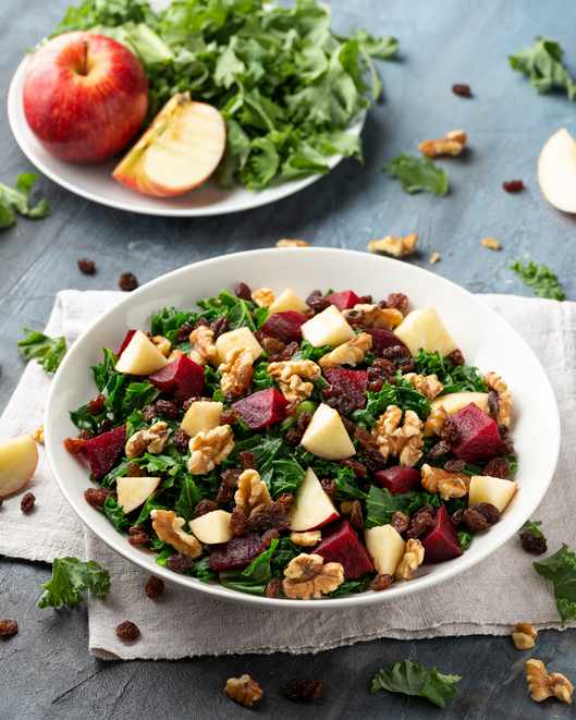 Kale salad with apple, beetroot, walnut and raisins in white plate. Healthy food.