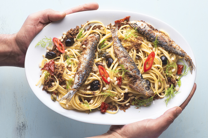Pasta with sardines,  typical dish of the Sicilian culinary tradition, poor kitchen recipe, white wine with raisins, pine nuts, bread crumbs, olive oil and wild  fennel, oval plate  in the chef hands