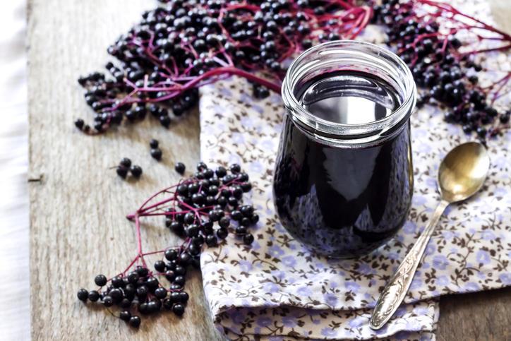 Homemade black elderberry syrup in glass jar and bunches of black elderberry in background