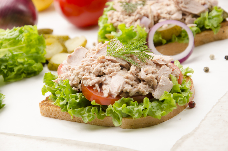 Tuna sandwiches with lettuce tomatoes and onions on parchment paper