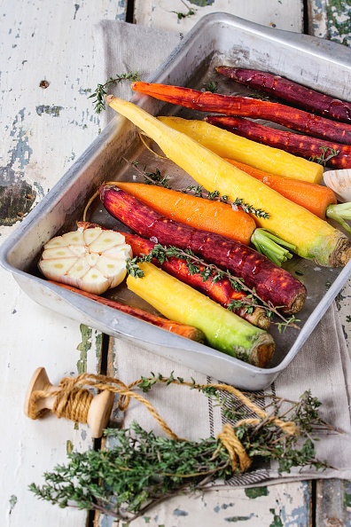 Ready for baking peeled colorful raw carrots with fresh thyme herbs and sliced garlic in aluminum tray over old white wooden surface. (Photo by: Natasha Breen/REDA&CO/Universal Images Group via Getty Images)