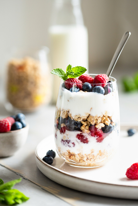 Glass of parfait made of granola, berries and yogurt on the table. Shot at angle, close up view, selective focus.