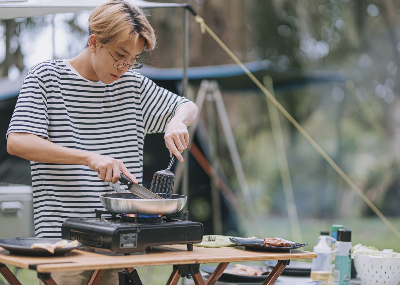 asian chinese teenage boy cutting pan fried chicken cooking for his family at camping tent