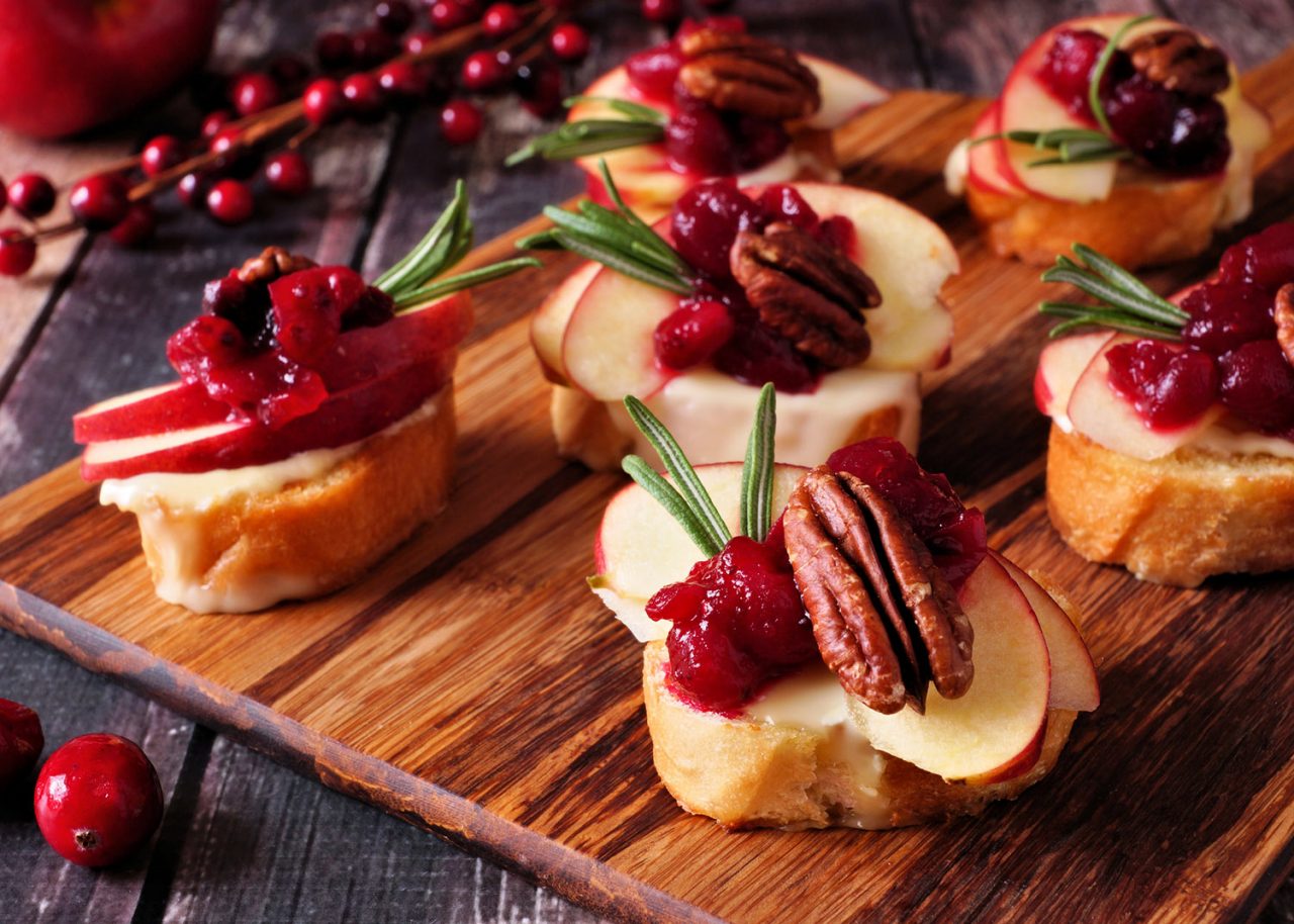 Crostini appetizers with apples, cranberries, brie and pecans. Close up table scene on a wooden platter.